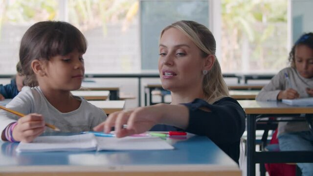 Primary school teacher helping Latin pupil girl drawing in her copybook at desk, checking and explaining task. Dolly shot. Education or teaching concept