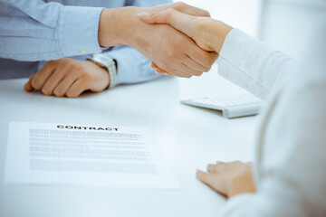 Obraz na płótnie Canvas Casual dressed businessman and woman shaking hands after contract signing in white colored office. Handshake concept