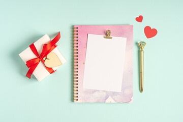Desktop blank paper note pad. Flat lay of blue pastel working table background with Valentine gift, letter, heart shape and decoration. Top view, mock up greeting card, notebook.