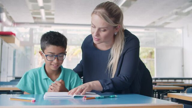 Friendly school teacher explaining task to pupil boy at desk, giving help to student. Dolly shot. Education or back to school concept