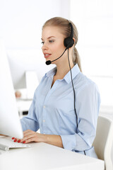 Blond woman call operator is using computer and headset for consulting clients online. Group of...