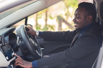 African man in a black suit sitting behind the wheel with smile and happy