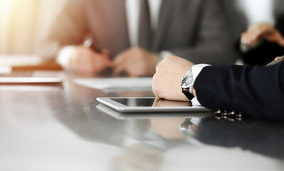 Unknown businessmen and woman sitting, using laptop computer and discussing questions at meeting in sunny office, close-up. Success concept