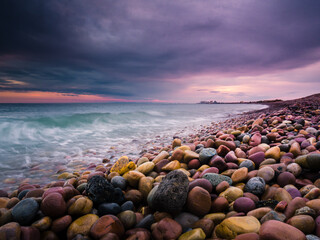 Playa de rocas al atardecer con cielo nuboso amenazando tormenta