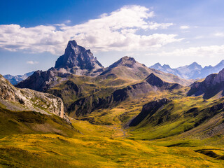 Montaña con forma de piramide destaca sobre el paisaje alpino de los Pirineos y el cielo azul con nubes blancas - obrazy, fototapety, plakaty