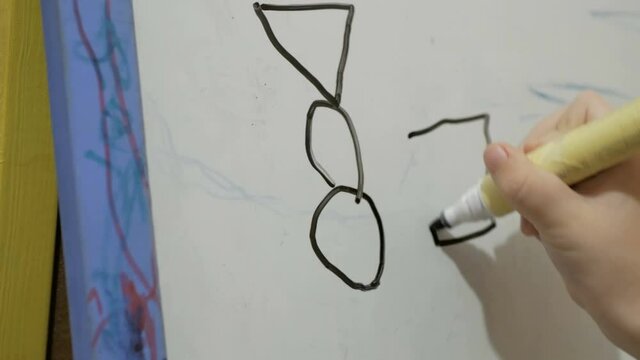 Close-up of a little girl's hand, she draws with a black flamaster on a white board.