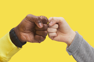 Graphic close up of two young people bumping fists against illuminating yellow background, interracial friendship and unity concept, copy space