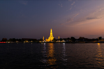 View of Illuminated Wat Arun Temple from the Chao Phraya river in sunset. Buddhist temple in Bangkok, Thailand