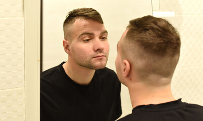 Young man looking in the mirror at his reflection in a bathroom
