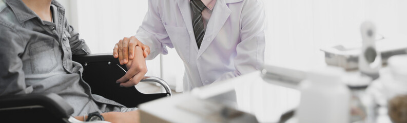 Asian doctor consulting and encourage disability young patient wheelchair person in doctor's office...