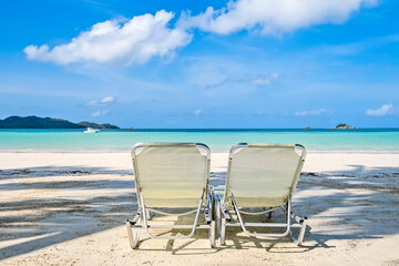 Two white beach chairs on tropical sandy beach