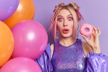 Surprised blonde young European woman stares bugged eyes at camera holds delicious glazed doughnut...