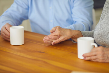 Married senior couple sitting at table, drinking tea and holding hands. Love, long marriage, happy relationship, family values, mutual respect and support, wellbeing of mature people concept. Close-up