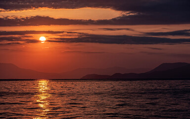 orange fiery sundown sky with some clouds over calm sea, scenic nature background