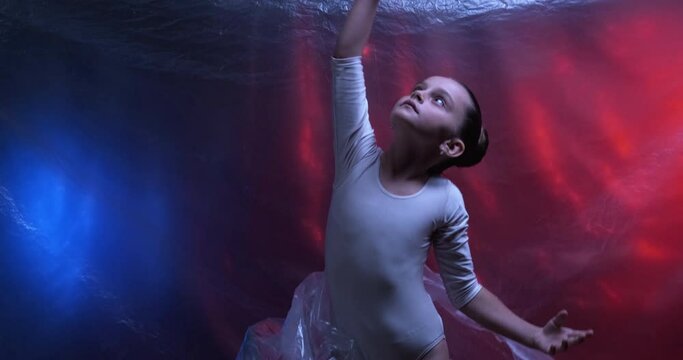 Child motivation. Kid hobby. Inspiration talent. Choreography performance. Small ballerina girl raising up from red darkness transparent polyethylene film to blue light on wrinkled texture background.