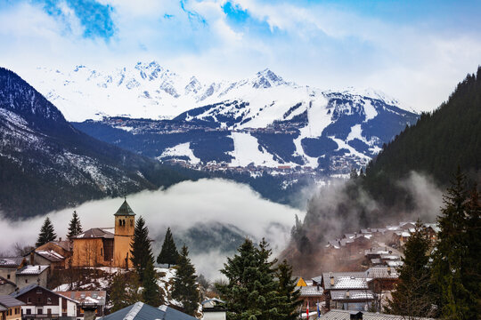 Champagny-en-Vanoise village panorama with mist and clouds around old church, over Courchevel resort on background