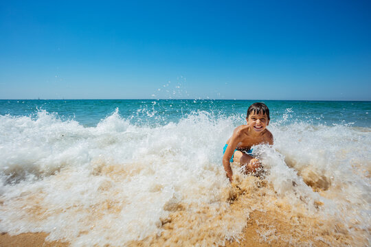 Action motion photo of a little boy play in splashing waves on the seashore sand beach