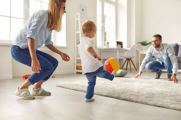 Happy young family with little son playing ball and having fun together at home with room interior...