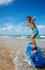 Photo of a boy riding surfboard on the beach during lesson practicing with his board in cute...