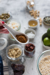 Woman hand holding a ceramic spoon full of ground cinnamon over some blurred granola ingredients.
