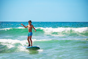 Cute small boy confidently ride waves on surfboard happy smiling and looking to camera