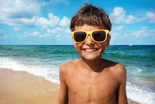 Close happy portrait of the smiling boy in sunglasses with beach on background