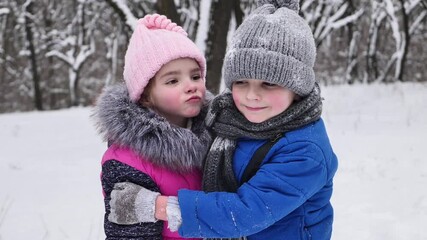 Beautiful little girl kisses a boy on the street in winter, in a snow-covered forest