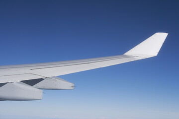 silberner Flügel eines Flugzeugs vor blauem Himmel