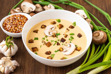 Mushroom cream soup on a wooden background with onions and croutons.