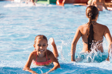 Little cheerful girl playing in the pool with clear and clear water and looking smiling at the camera