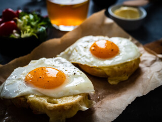 Continental breakfast - sunny side up eggs on baked bun with cheese and vegetable salad on black background
