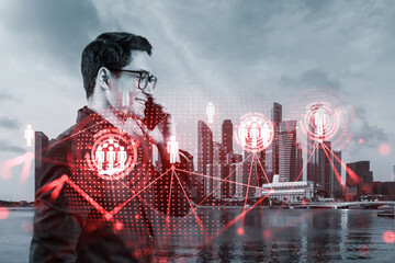 A young handsome eastern businessman processing conference call to develop social media marketing strategy to achieve business goals. Hologram icons over Singapore background.
