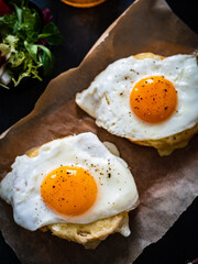 Continental breakfast - sunny side up eggs on baked bun with cheese and vegetable salad on black background
