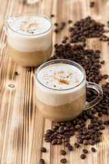 Two delicious cappuccinos sprinkled with chocolate chips on a wooden background with coffee beans.