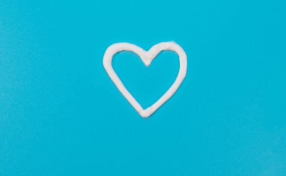 
White heart shape created from cream on light pastel blue background, top view. Valentine's day background.