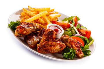 Roast chicken wings with curly fries and vegetable salad on white background

