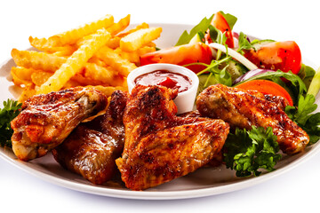 Roast chicken wings with curly fries and vegetable salad on white background
