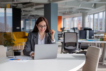 Young smiling businesswoman working at the laptop in open space office.