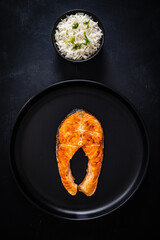Fried salmon steak with basmati rice served on black background