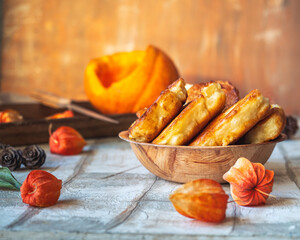 Deep plate with pumpkin pancakes, cut pumpkin and dried flowers and a branch with berries