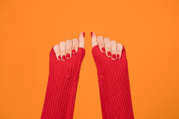 Female hands raised up on orange background. Red sweater and red fingernails. Freedom symbol.