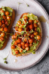 
bruschetta with avocado, chickpeas and microgreens on a dark background