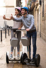 young couple guy and girl walking on segway in streets of european city