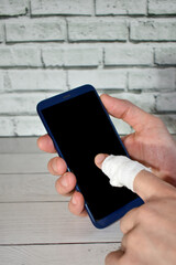 mans hand with bandaged finger holds smartphone to call an ambulance. Accident at work. Close-up Smartphone in hand. call for help, health insurance. mobile app concept