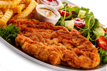 Breaded fried pork chop, French fries and vegetables on white background
