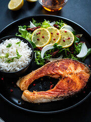 Fried salmon steak with basmati rice and  mix of vegetables served on black plate on wooden table
