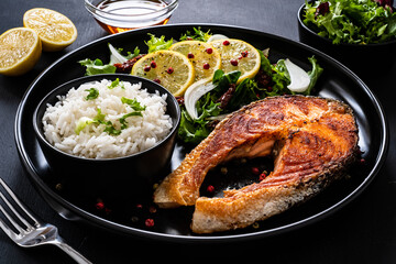 Fried salmon steak with basmati rice and  mix of vegetables served on black plate on wooden table