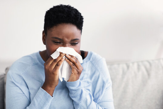 Sick black woman sneezing, holding tissue paper