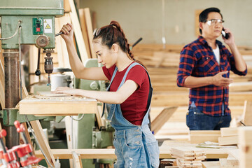 Concentrated young Asian carpenter setting milling cutter above wooden board