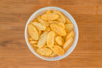 Heap of dried baguettes in a white bowl. Top view on blurred wooden bamboo background.
